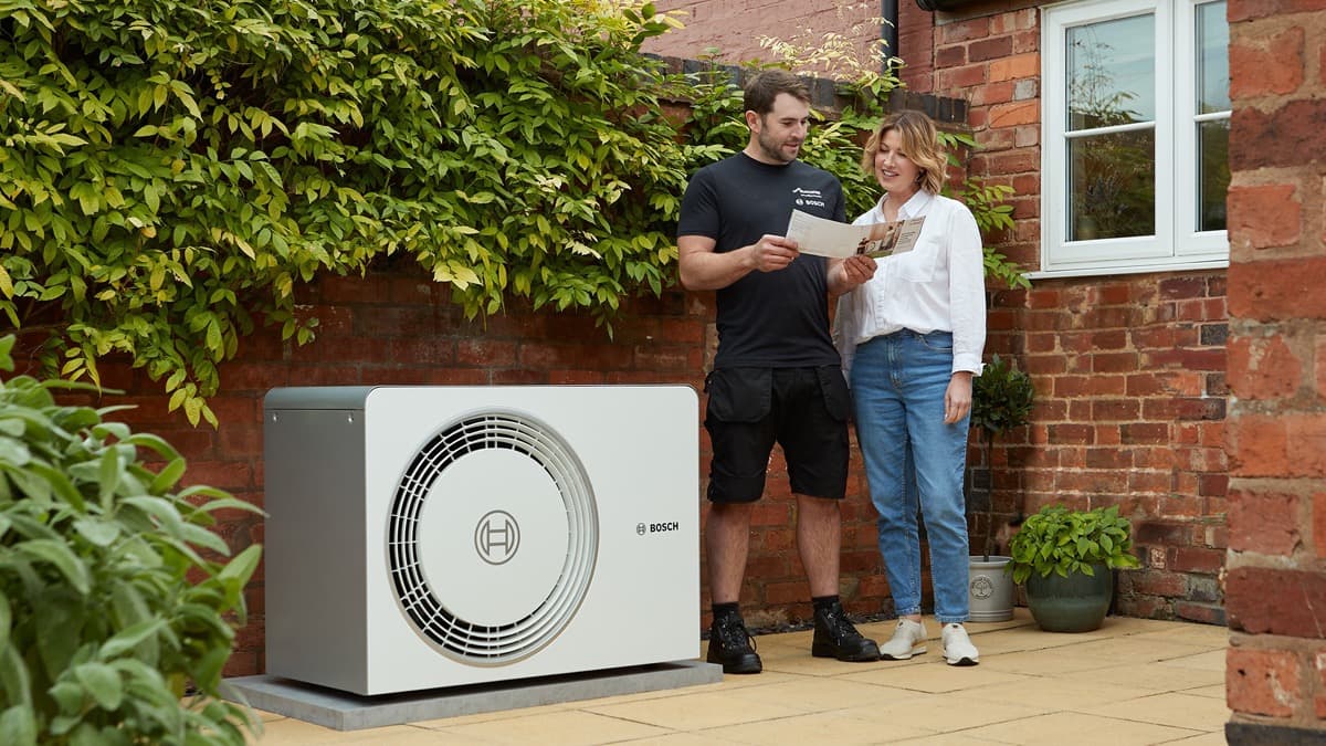 Heating engineer and homeowner reviewing installation documentation beside a new heat pump